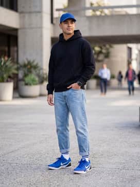 Kobe Ix Elite Low Em Protro – A streetwear-inspired look consisting of light-wash tapered jeans, an oversized black graphic hoodie, and a royal blue cap to coordinate with the footwear.