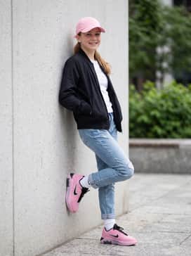 Distressed light-wash slim jeans with an oversized white graphic tee and a matching pink cap for a casual urban look.