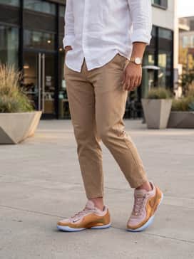 A clean smart-casual ensemble consisting of tapered tan chinos, a crisp white button-down linen shirt left untucked, and a gold-tone watch to mirror the sneaker's metallic hardware.