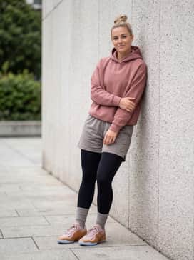 A high-performance athletic outfit with black moisture-wicking compression tights, mesh basketball shorts in a neutral grey, and a breathable tech-fleece hoodie in a muted rose shade.