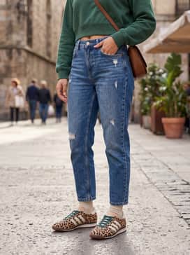 Distressed blue mom jeans styled with a cropped forest green sweatshirt that complements the teal laces, finished with a sleek leather crossbody bag.
