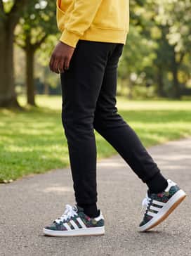 Slim-fit black joggers styled with a bright yellow hoodie that echoes the small yellow sun-like motifs within the shoe's pattern.