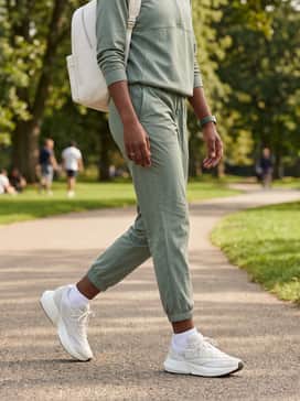 An elevated athletic set featuring sage green nylon joggers and a matching technical quarter-zip pullover, finished with a minimalist leather backpack.