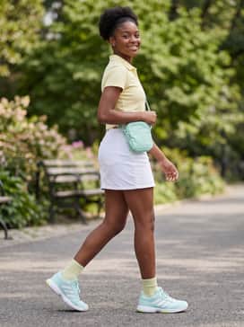 A fresh summer streetwear style with a white denim mini-skirt, a pastel yellow cropped polo shirt, and a small nylon crossbody bag.