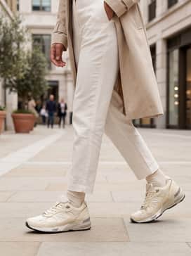 Straight-leg light-wash vintage denim jeans with a tucked-in white ribbed tank and a structured camel-colored trench coat.