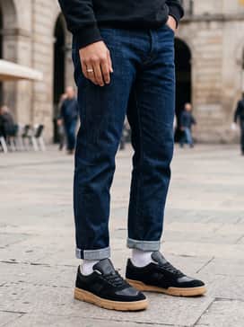Style with cuffed indigo raw denim, a white heavyweight tee, and an olive-toned utility jacket for a rugged, heritage-inspired outfit.