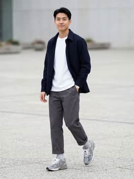A refined streetwear ensemble featuring charcoal grey relaxed-fit trousers, a crisp white heavyweight t-shirt, and an unbuttoned navy blue wool overshirt.