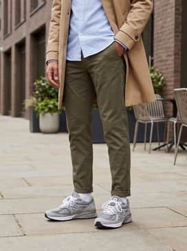 A smart-casual look consisting of slim-tapered olive chinos, a tucked-in light blue oxford button-down, and a tan trench coat for a sophisticated urban vibe.