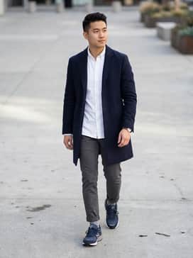 Slim-fit charcoal grey chinos paired with a crisp white Oxford shirt and a navy wool overcoat for a sophisticated city look.
