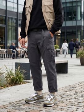 Charcoal grey technical cargo pants worn with a black oversized hoodie and a beige utility vest to lean into the functional gorpcore trend.