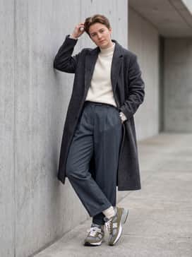 Wide-leg pleated trousers in a slate grey, paired with a tucked-in cream mock-neck sweater and a long wool overcoat for a sophisticated streetwear look.