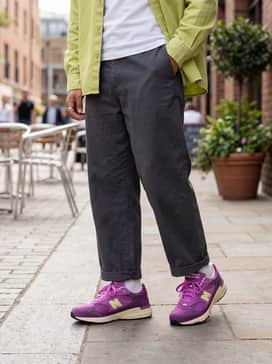 Charcoal grey wide-leg trousers and a tucked-in white baby tee, layered with an unbuttoned lime green overshirt to complement the vibrant 'N' logo.