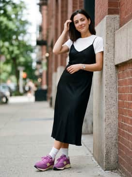 A black midi slip dress worn over a white t-shirt for a 90s-inspired look, finished with white crew socks to bridge the gap between the dress and the chunky sneaker.