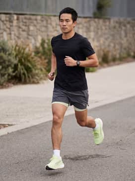 A pair of charcoal grey 5-inch inseam running shorts paired with a black moisture-wicking performance tee and low-cut white athletic socks.