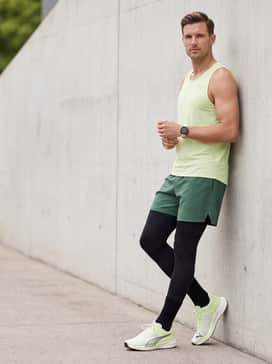 Black compression tights worn under forest green breathable athletic shorts with a matching lime green singlet to echo the shoe's color.