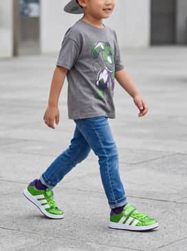 A Marvel character graphic t-shirt paired with relaxed-fit blue denim jeans and a matching green baseball cap.