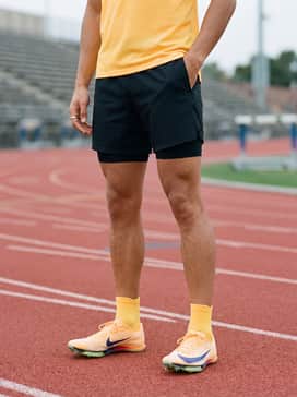 Maxfly 2 – Lightweight black mesh running shorts paired with a breathable volt-orange moisture-wicking singlet for a coordinated look.
