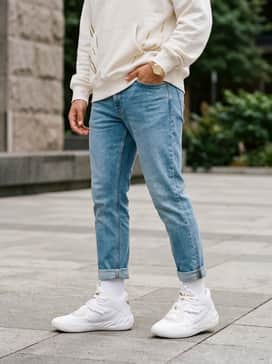 A streetwear-inspired ensemble with tapered light-wash slim jeans, an oversized white hoodie with metallic gold graphics, and a gold-tone luxury watch.