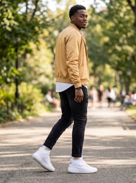 A bold evening streetwear look pairing black distressed denim with a white drop-hem t-shirt and an unbuttoned gold satin bomber jacket.