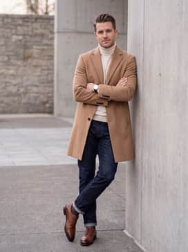 Dark indigo selvedge denim with a slight cuff, a cream cashmere turtleneck sweater, and a tailored camel overcoat for a sophisticated smart-casual winter aesthetic.