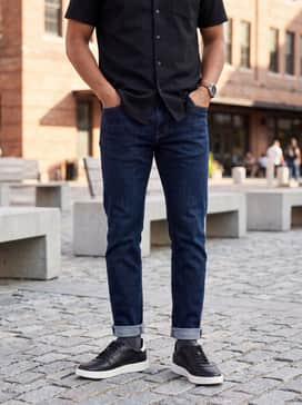 Mens Grand Crosscourt Daily Court Sneakers – Dark wash indigo denim jeans with a small cuff, styled with a grey heather cashmere sweater and a tailored black wool topcoat.
