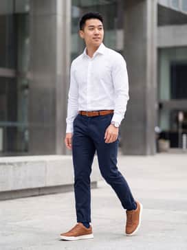 Slim-fit navy blue chinos paired with a crisp white button-down shirt and a matching cognac leather belt for a cohesive office-ready look.