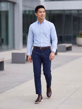 Navy tailored chinos paired with a light blue button-down oxford shirt and a matching dark brown leather belt for a classic business casual look.