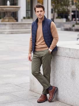 Olive green tailored trousers matched with a tan cashmere sweater and a lightweight quilted navy vest for a sophisticated autumn weekend aesthetic.