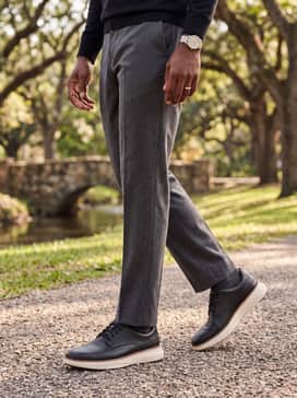 Charcoal grey tailored wool trousers and a black turtleneck sweater, creating a sleek, monochromatic ensemble that highlights the contrast of the cream sole.