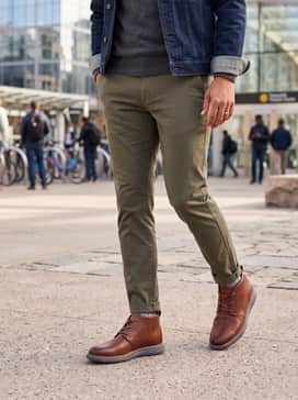 Tapered olive green chinos worn with a heather grey cashmere crewneck sweater and a denim jacket for a balanced, rugged-yet-clean ensemble.
