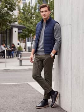 Tapered olive green trousers combined with a heather grey crewneck sweater and a navy quilted vest for a polished yet functional weekend ensemble.