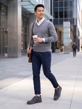 Mens Zergrand Remastered Stitchlite Wingtip Oxfords – Slim-fit navy chinos paired with a crisp white button-down shirt and a lightweight grey merino wool v-neck sweater for a polished office look.