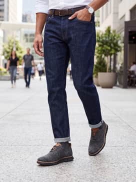 Dark indigo selvedge denim jeans with a neat cuff, a charcoal heather t-shirt, and an unlined navy blazer for a sophisticated weekend ensemble.