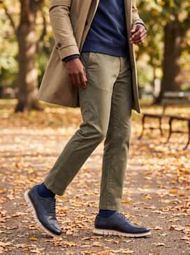 Olive green tailored trousers with a navy crewneck sweatshirt and a khaki trench coat for a sophisticated, high-low streetwear aesthetic.