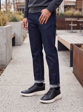 Dark indigo straight-leg denim jeans rolled at the cuff, worn with a grey crewneck cashmere sweater over a white tee for a refined weekend look.