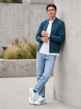 An off-duty streetwear outfit with light-wash slim-fit denim jeans cuffed at the ankle, a boxy white graphic t-shirt, and a deep teal bomber jacket to match the ASICS side stripes.