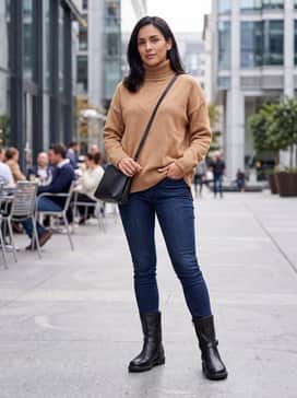 Metropole Amsterdam – Dark wash skinny jeans tucked into the boots, paired with an oversized camel-colored turtleneck sweater and a crossbody leather bag.