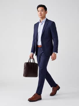 A navy blue tailored slim-fit suit paired with a light blue patterned shirt and a matching cognac leather belt for a sharp, authoritative office look.