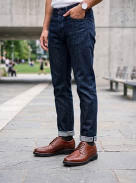 Metropole London – Dark wash straight-leg denim jeans with a neat cuff, a cream-colored cashmere turtleneck, and a navy wool pea coat for a classic autumnal ensemble.