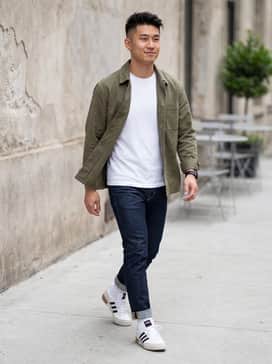Dark wash slim-fit jeans paired with a crisp white crewneck t-shirt and an unbuttoned olive green overshirt for a layered, versatile urban look.
