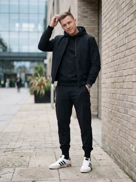 Black technical jogger pants with a fitted black hoodie and a structured bomber jacket, leaning into a sleek, monochrome streetwear aesthetic.