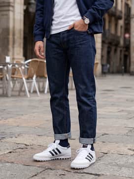 Tapered dark indigo denim jeans paired with a crisp white polo shirt and a navy Harrington jacket for a classic British terrace look.