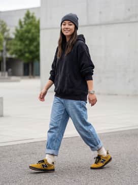 A pair of baggy light-wash denim jeans rolled at the cuff, paired with an oversized black graphic hoodie and a charcoal grey beanie for a quintessential skate look.