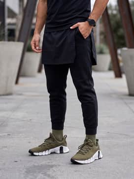 Nike Free Metcon 6 – A modern streetwear ensemble with tapered black tech-fleece joggers, an oversized white graphic t-shirt, and an olive green utility vest.