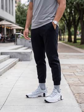 A clean athleisure ensemble with tapered black tech-fleece joggers, a white oversized graphic t-shirt, and a lightweight grey hoodie for transition wear.