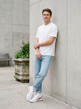 Light wash slim-cut denim jeans rolled at the cuff, a basic white heavyweight cotton tee, and a silver sports watch for a clean, everyday street style.