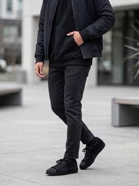 Black slim-fit jeans combined with an oversized graphic hoodie in a neutral tone and a structured bomber jacket for an elevated streetwear aesthetic.