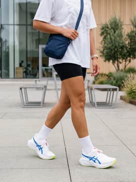 Modern gym-to-street ensemble: Black high-waisted bike shorts styled with an oversized white graphic tee and a sleek navy blue crossbody bag.