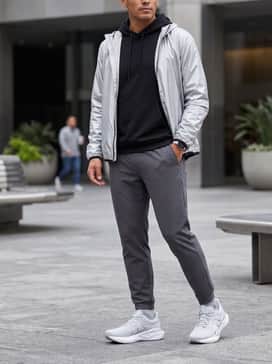Novablast 5 Atc – A sophisticated athleisure ensemble with charcoal grey tapered joggers, a fitted black performance hoodie, and a lightweight metallic silver windbreaker that echoes the shoe's accents.
