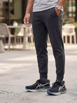 Novablast 5 Luxe – An urban athleisure look with tapered black tech-fleece joggers, an oversized charcoal hoodie, and a matte black baseball cap.